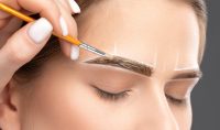 Make-up artist makes markings with white pencil for eyebrow and paints eyebrows. Professional makeup and facial care.